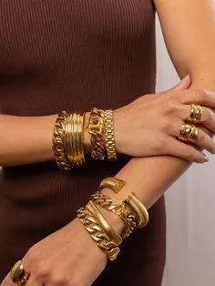 Hand holding a clutch, adorned with stacked rings and a chunky bracelet.